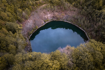 Small blue crater lake of a dormant volcano surrounded by forest in autumn colors in Germany