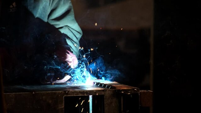 Factory worker welds metal. The man is welding. Welding with argon or electrode, using a welding machine. An industrial enterprise producing metal structures. Sparks and flashes fly. Slow motion