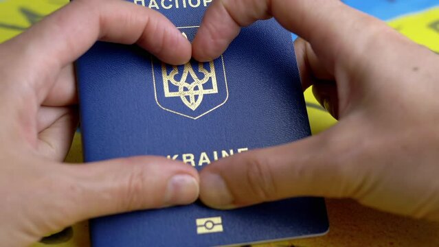 Hands in Shape of Heart Hold a Biometric Passport of Ukraine on Background Flag. Inscription in Ukrainian Ukraine Passport. Drawings of blue and yellow flags of Ukraine with messages stop the war.