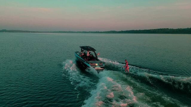 Drone view of a young sporty girl on wakesurfing on boat with leaving trail on water surface