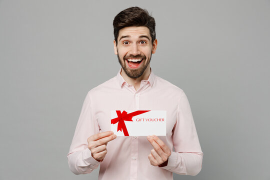 Young Shocked Excited Amazed Caucasian Man 20s He Wear Basic White Shirt Hold Gift Certificate Coupon Voucher Card For Store Isolated On Plain Grey Background Studio Portrait People Lifestyle Concept