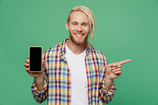 Young caucasian blond man with dreadlocks he wear casual shirt hold in hand use mobile cell phone with blank screen workspace area point finger aside isolated on pastel plain light green background. - Powered by Adobe