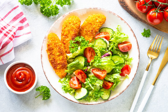 Chicken nuggets with green vegetable salad and ketchup sauce at white table. Healthy food. Top view image with copy space,