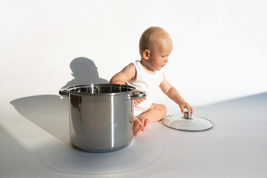 Child cook, food boy. Little cute baby chef sitting near big cooking pot with kitchen, utensils, accessories on white background. Copy space