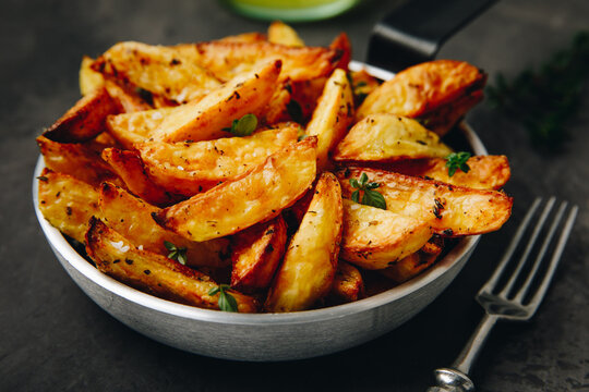 Roasted potatoes. Baked potato wedges in frying pan on dark background.