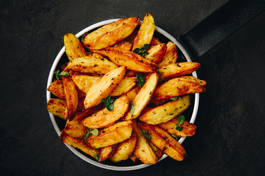 Roasted potatoes. Baked potato wedges in frying pan on dark stone background.