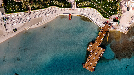 Aerial drone view to the beach with white sand, pier with sunchairs and sea. Luxury summer vacation and resort.