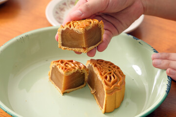traditional Chinese moon cake mid autumn festival verity design colour green yellow cut slice held by beautiful  female hand on rustic plates over wooden table