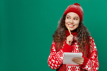 Merry young woman wear red warm cozy knitted sweater hat posing write in notebook plan look aside...