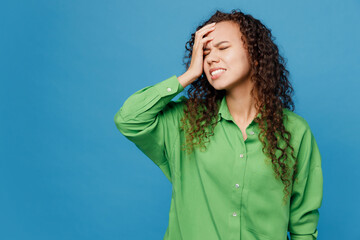 Young woman of African American ethnicity 20s she wear green shirt put hand on face facepalm epic fail mistaken omg gesture isolated on plain blue background studio portrait. People lifestyle concept.