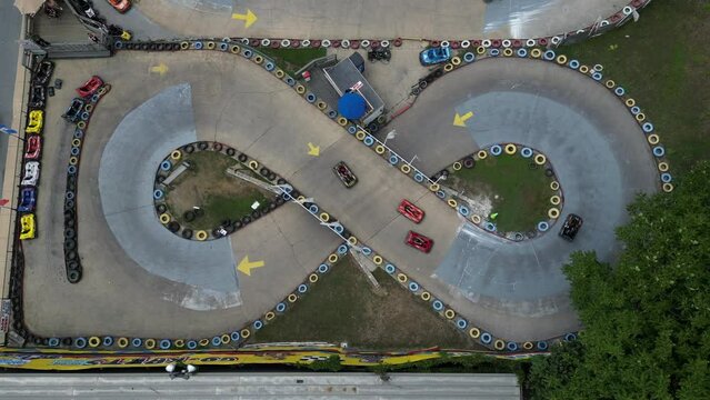 A top down view, directly above a go-kart race track in the shape of the number eight. It was shot on a sunny day where the drone camera is stationary as the cars race around the small track.
