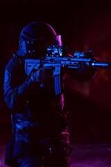 Fototapeta na wymiar Army soldier in Combat Uniforms with an assault rifle and combat helmet night mission dark background. Blue and purple gel light effect. 