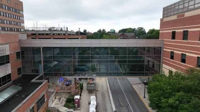 Descending Aerial Footage Reveals City Sky Bridge Connecting Two Buildings. Foggy Sky Over City Streets. Indoor Bridge Allows Walkability And Accessibility In All Weather Conditions.