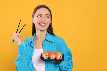 Happy young woman with plate of sushi rolls and chopsticks on orange background. Space for text