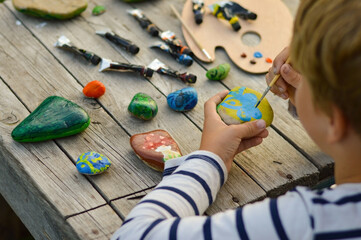 A detailed picture of a child's hands drawing a fungus on a stone with acrylic paints. Home hobbies are authentic. Artwork on stones.