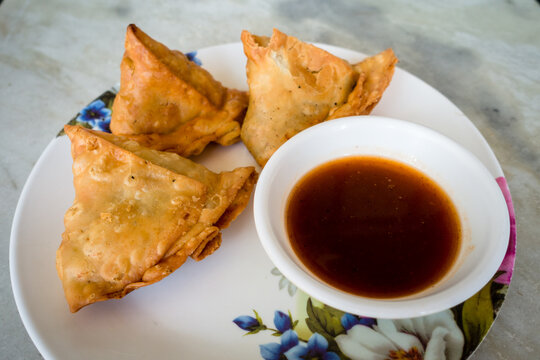 Samosa with tamarind sauce or chutney. A samosa or singara is a fried or baked pastry with a savory filling, including ingredients such as spiced potatoes, onions, and peas. Uttarakhand India.