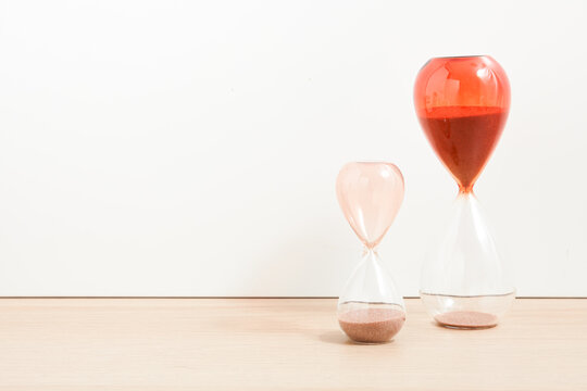 Hourglass isolated on wood background. Minimalist hourglass design. Product design. Scandinavian style. Home decoration. Timer. Timber background. Orange and pink hourglass.