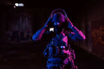 Army soldier in Combat Uniforms with an assault rifle and combat helmet night mission dark background. Blue and purple gel light effect. 