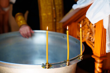three burning candles on the font for baptism in the Orthodox Church.
