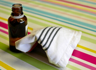 A bottle of essential oil and a white tissue are placed on a multicolored background.