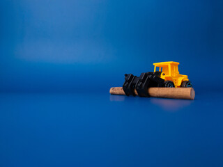 Naklejka premium Excavator with wooden stick on blue background with copy space. Conceptual image of illegal logging.