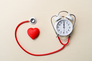 Timely diagnosis of cardiac diseases. Heart next to an alarm clock and a stethoscope on a yellow...