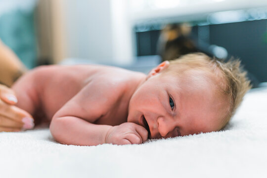 Portrait of newborn baby boy with blond hair having his diaper changed lying on blanket on floor with uncomfortable expression. Horizontal close-up indoor shot. High quality photo