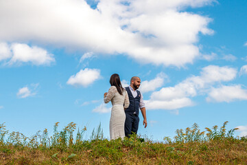 beautiful girl in a white dress and a guy in a field against a blue sky with clouds