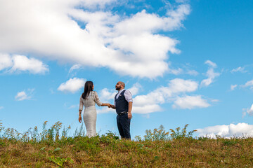 beautiful girl in a white dress and a guy in a field against a blue sky with clouds
