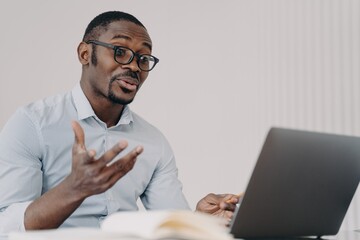 African american businessman in glasses discussing working project by video call at laptop - obrazy, fototapety, plakaty