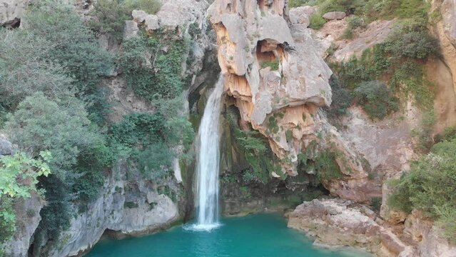 Aerial elevating shot over a spectacular waterfall, skull shape rock, as the power of nature formed a clear green lake in the mountains.