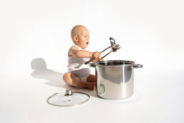 Child cook, food boy. Little cute baby chef holding spoon sitting near big cooking pot with kitchen, utensils, accessories on white background. Copy space