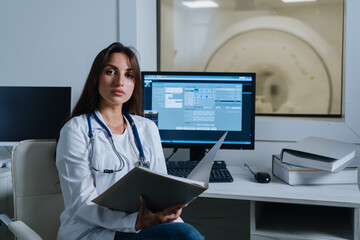 Portrait of a radiologist doctor who is sitting at a table with a patient's medical record. A young...