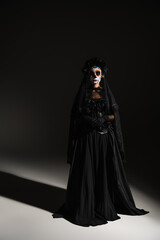 Naklejka premium full length of woman in mexican day of dead costume and spooky makeup on black background.