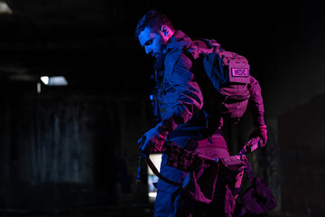 Army soldier in Combat Uniforms with an assault rifle and combat helmet night mission dark background. Blue and purple gel light effect. 