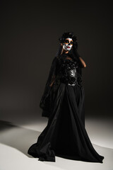 full length of woman in sugar skull makeup and dark dress with veil on black background.