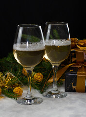 In the atmosphere of Christmas, spruce branches, boxes with gifts and New Year's toys lie on the snow. In the foreground are two crystal glasses with alcohol December holidays concept.