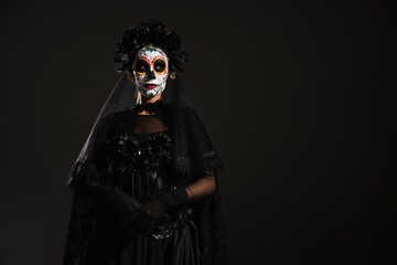 woman in dark and scary costume and sugar skull makeup standing isolated on black.