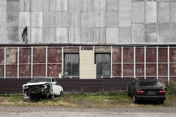 Old broken cars near the wall of the house. On the wall there is an inscription in Russian "DANGER ZONE". Dirty building wall with damaged cladding.