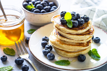 Pancakes stack with fresh blueberries and honey at white stone table.