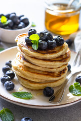 Pancakes stack with fresh blueberries and honey at white stone table.
