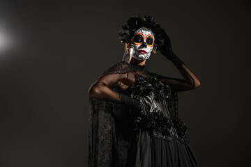 low angle view of woman in sugar skull makeup and halloween costume posing with hand on hip on...