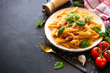 Pasta with tomato sauce, basil and parmesan cheese on dark table. Penne pasta with tomato sauce alla arrabbiata with ingredients.