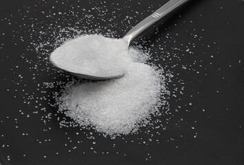 Spoonful of sugar on a black plate.