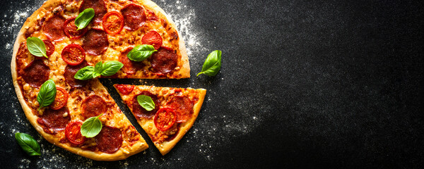 Pizza on black background. Traditional italian pizza with salami cheese, tomatoes and basil. Long banner format.