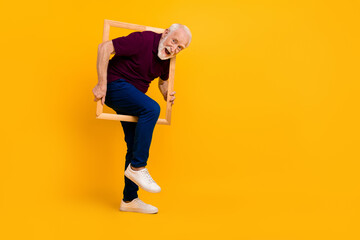 Fototapeta na wymiar Full size profile side photo of cheerful senior man have fun make picture wood frame isolated over yellow color background