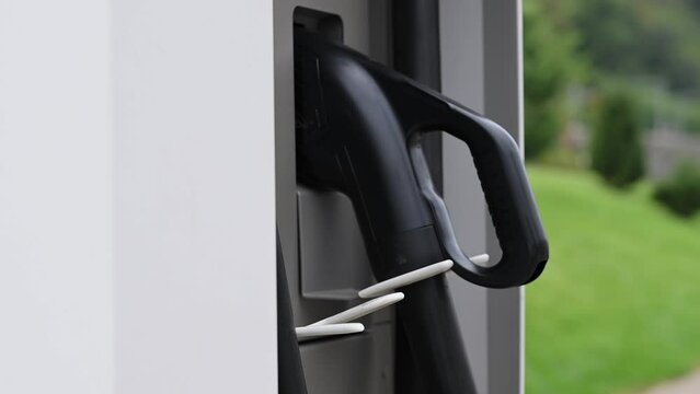 Close-up of young woman's hand taking charging port of electric car at public charging station. Ecology conservation concept, future technologies, electric vehicles, alternative energy. Slow motion