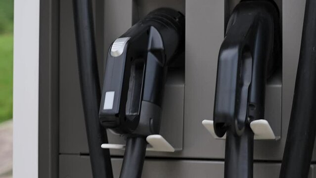 Close-up of young woman's hand puts an electric car charging port at public charging station. Ecology conservation concept, future technologies, electric vehicles, alternative energy Slow motion