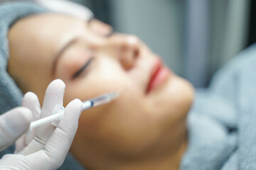 Closeup and crop hand of beauty doctor in medical grove holding beauty skin syringe injecting the customer's face. Beauty skin concept, selective focus on doctor's hand.