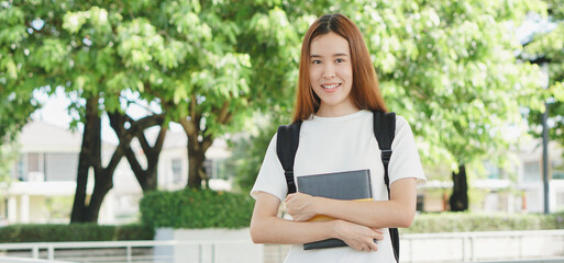 Portrait of asian female colleges student holding textbook in her hands and standing outdoors at...